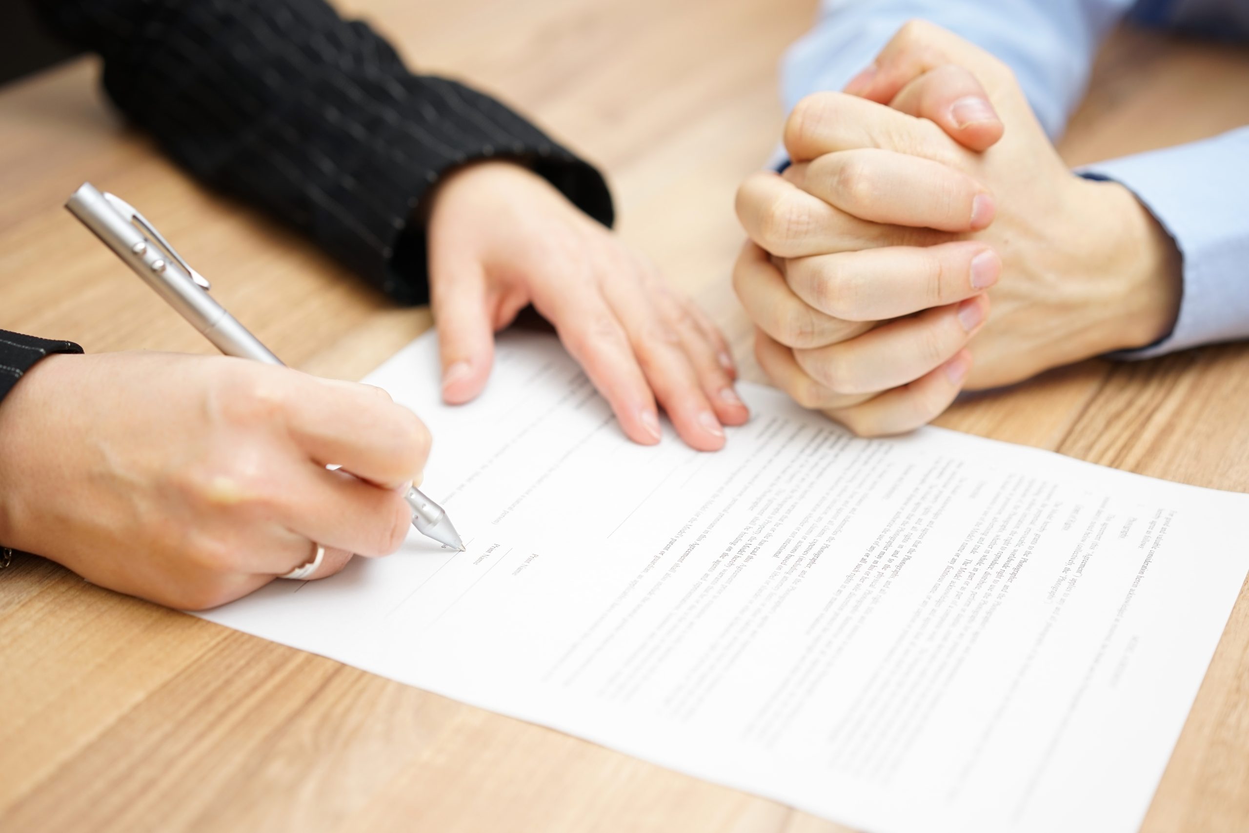 Clasped hands of a man and woman with a wedding ring signing paperwork - About Us | Family Funeral Funding