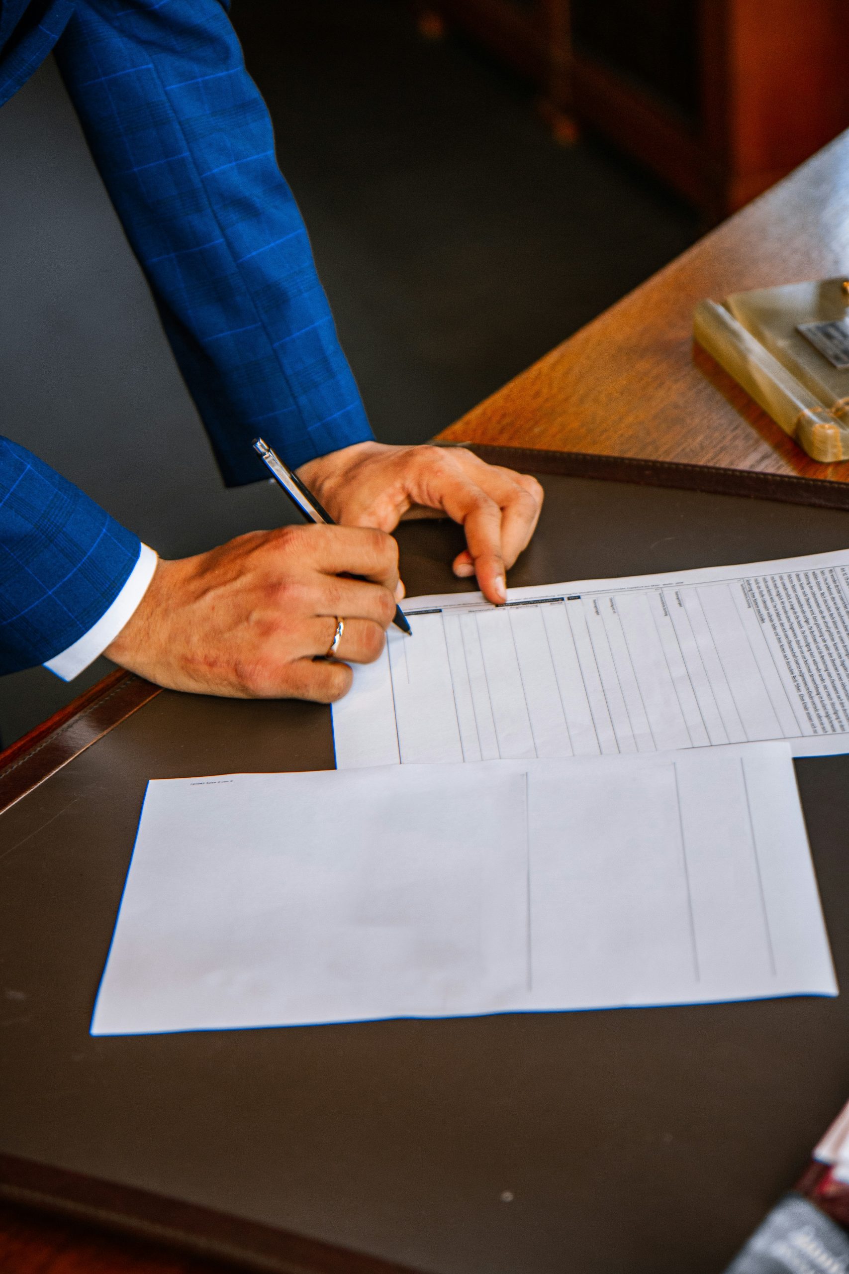 Man in blue suit signing paperwork at a wooden desk | What Is a Funeral Home Assignment Form and Who Signs It? - Family Funeral Funding: Life Insurance Assignment Funding for Funeral Homes | Insurance Assignments