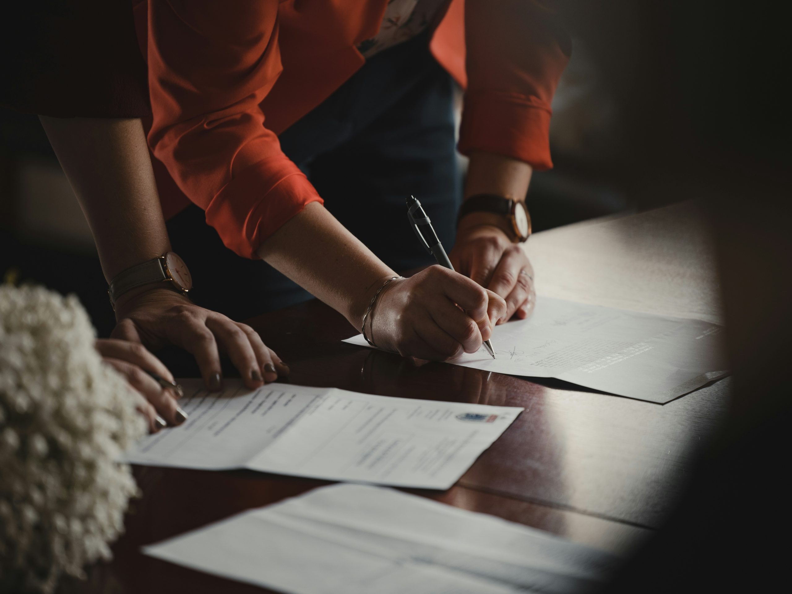 Woman signing paperwork on a wooden desk | Family Funeral Funding: Assignment in Insurance for Funeral Homes | Insurance Claims & Insurance Assignments